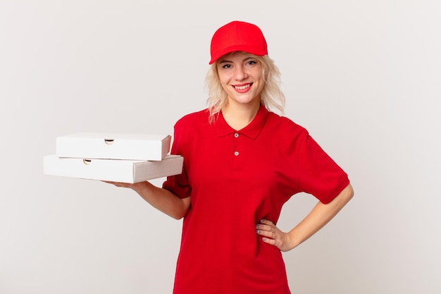 Mujer bonita joven sonriendo felizmente con una mano en la cadera y confiada. concepto de entrega de pizza