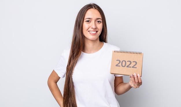 Mujer bonita joven sonriendo felizmente con una mano en la cadera y confiada. Concepto de planificador 2022