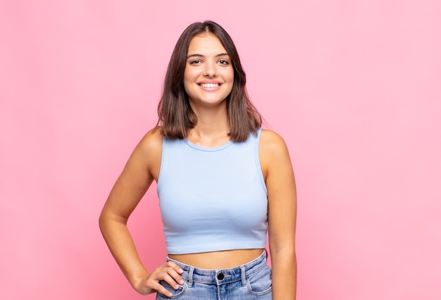 Mujer bonita joven sonriendo felizmente con una mano en la cadera y seguro