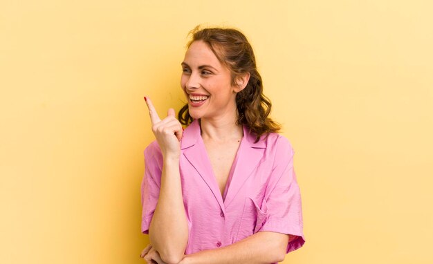 Mujer bonita joven sonriendo felizmente y mirando hacia los lados preguntándose si pensar o tener una idea