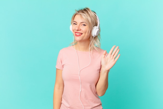 Mujer bonita joven sonriendo felizmente, saludando con la mano, dándote la bienvenida y saludándote. escuchando musica concepto