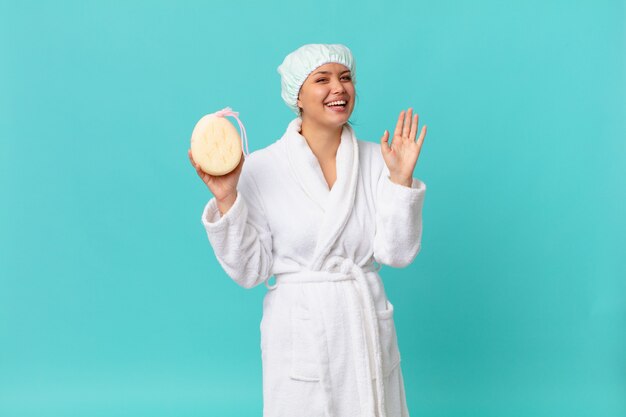 Mujer bonita joven sonriendo felizmente, saludando con la mano, dándote la bienvenida y saludándote y vistiendo una bata de baño después de la ducha