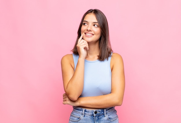 Mujer bonita joven sonriendo felizmente y soñando despierta o dudando, mirando hacia un lado