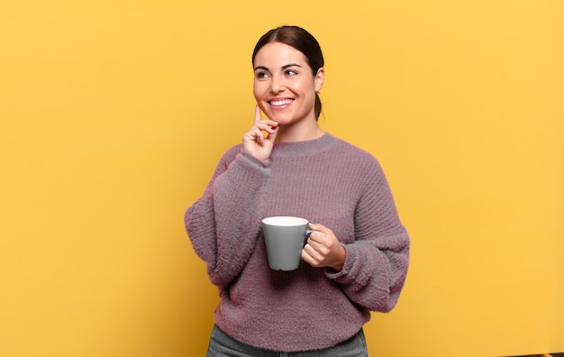 Mujer bonita joven sonriendo felizmente y soñando despierto o dudando, mirando hacia el lado