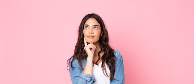 Mujer bonita joven sonriendo felizmente y soñando despierto o dudando, mirando hacia el lado