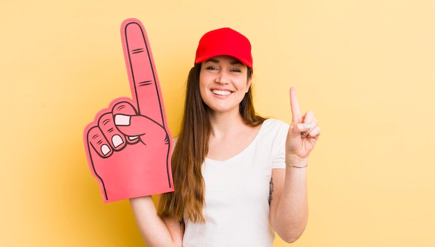 Mujer bonita joven sonriendo y luciendo amable mostrando el concepto de mano número uno número uno