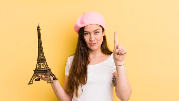 Mujer bonita joven sonriendo y luciendo amigable mostrando el concepto número uno de París