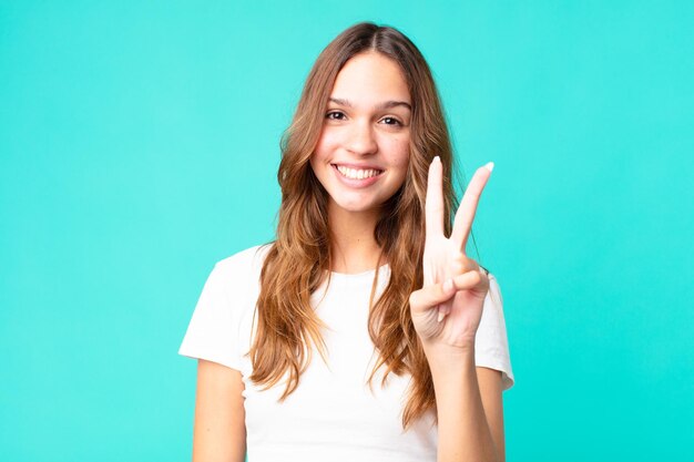 Mujer bonita joven sonriendo y luciendo amigable mostrando el número dos