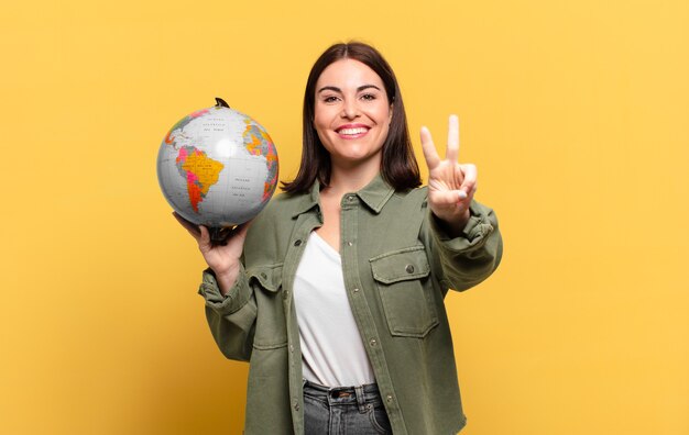 Mujer bonita joven sonriendo y luciendo feliz, despreocupada y positiva, gesticulando victoria o paz con una mano