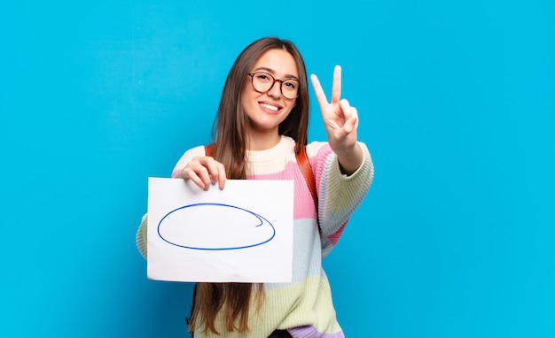 Mujer bonita joven sonriendo y luciendo feliz, despreocupada y positiva, gesticulando victoria o paz con una mano