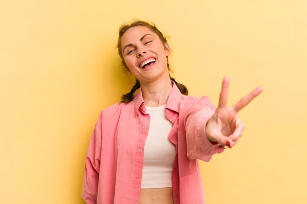 Mujer bonita joven sonriendo y luciendo feliz despreocupada y positiva gesticulando victoria o paz con una mano