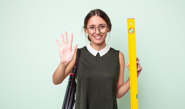 Mujer bonita joven sonriendo y mirando amigable, mostrando el número cinco. concepto de arquitectura