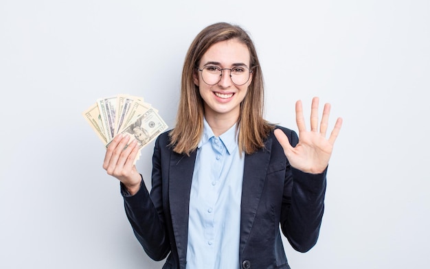 Mujer bonita joven sonriendo y mirando amigable, mostrando el número cinco. concepto de billetes de dólar