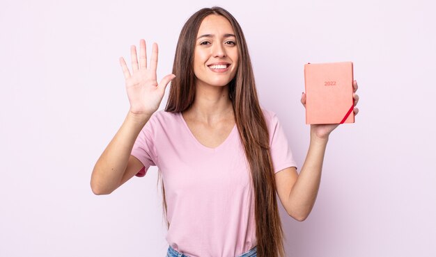 mujer bonita joven sonriendo y mirando amigable, mostrando el número cinco. Concepto de planificador 2022