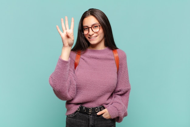 Mujer bonita joven sonriendo y mirando amigable, mostrando el número cuatro o cuarto con la mano hacia adelante, contando hacia atrás. concepto de estudiante