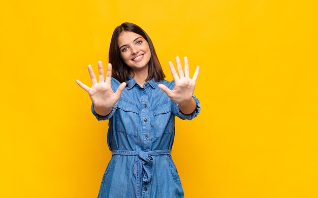 Mujer bonita joven sonriendo y mirando amigable, mostrando el número diez o décimo con la mano hacia adelante, contando hacia atrás