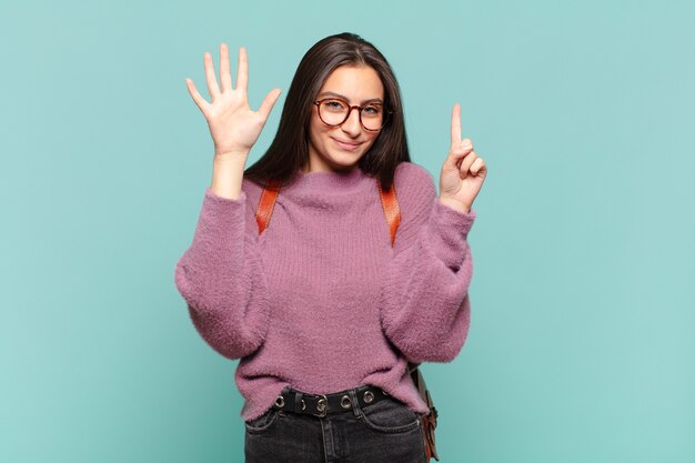 Mujer bonita joven sonriendo y mirando amigable, mostrando el número seis o sexto con la mano hacia adelante, contando hacia atrás. concepto de estudiante