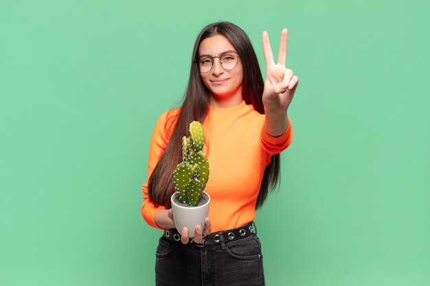 Mujer bonita joven sonriendo y mirando amistosamente, mostrando el número dos o el segundo con la mano hacia adelante, contando hacia atrás. concepto de cactus