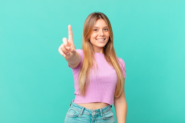 Mujer bonita joven sonriendo con orgullo y confianza haciendo el número uno