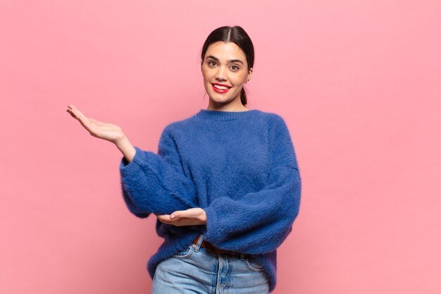 Mujer bonita joven sonriendo con orgullo y confianza, sintiéndose feliz y satisfecho y mostrando un concepto en el espacio de la copia