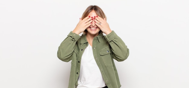 Foto mujer bonita joven sonriendo y sintiéndose feliz, cubriéndose los ojos con ambas manos y esperando una sorpresa increíble