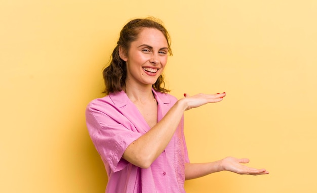 Mujer bonita joven sonriendo sintiéndose feliz positiva y satisfecha sosteniendo o mostrando un objeto o concepto en el espacio de la copia