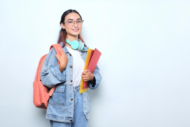 Mujer bonita joven sonriente que lleva una mochila que sostiene los libros aislados en el fondo blanco