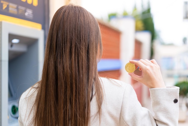 Mujer bonita joven sosteniendo un Bitcoin al aire libre en posición trasera