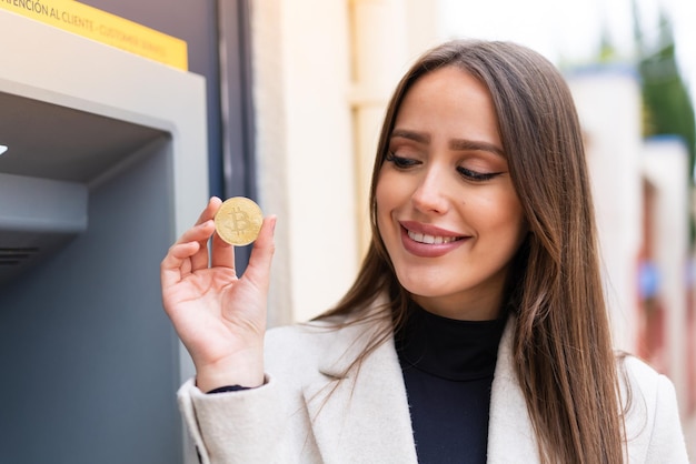 Mujer bonita joven sosteniendo un Bitcoin al aire libre