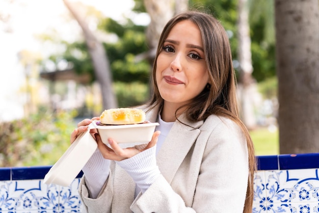 Mujer bonita joven sosteniendo una hamburguesa al aire libre