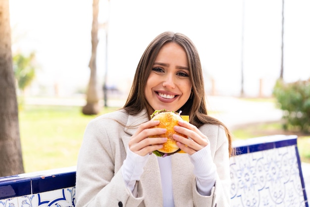 Mujer bonita joven sosteniendo una hamburguesa al aire libre