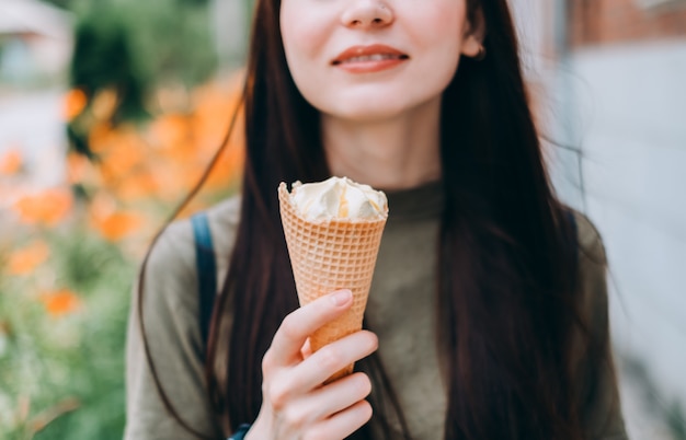 Mujer bonita joven sosteniendo helado en un cono de galleta mientras camina en el parque.