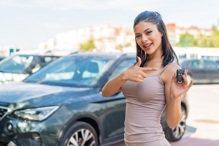 Foto mujer bonita joven sosteniendo las llaves del auto al aire libre y apuntándolo