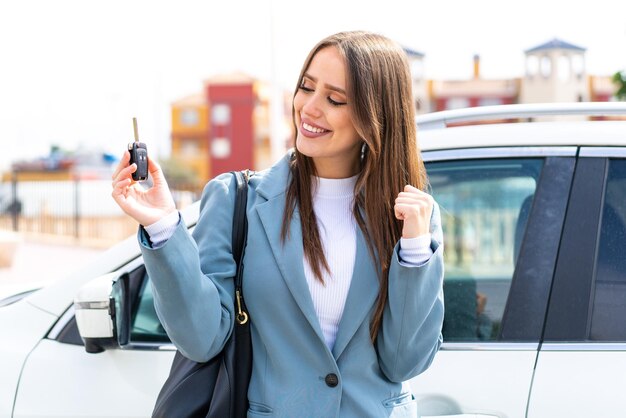 Mujer bonita joven sosteniendo las llaves del auto al aire libre celebrando una victoria