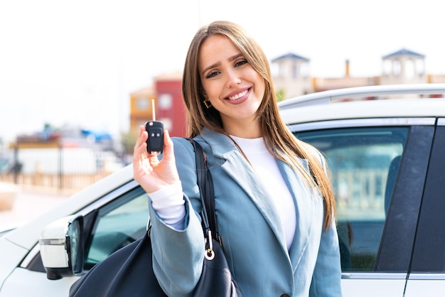 Mujer bonita joven sosteniendo las llaves del auto al aire libre con expresión feliz