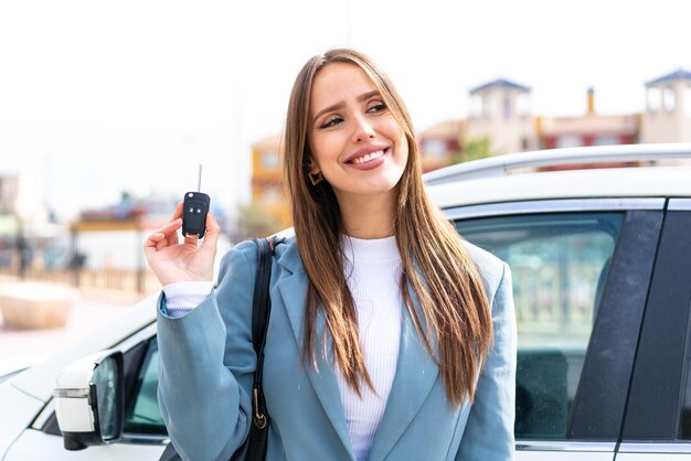 Mujer bonita joven sosteniendo las llaves del auto al aire libre mirando hacia arriba mientras sonríe