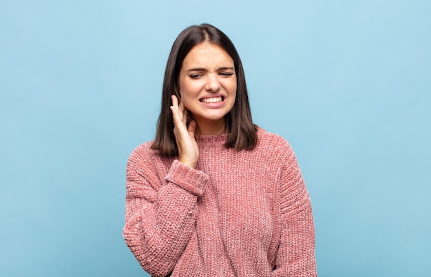 Mujer bonita joven sosteniendo la mejilla y sufriendo dolor de muelas doloroso, sintiéndose enferma, miserable e infeliz, buscando un dentista