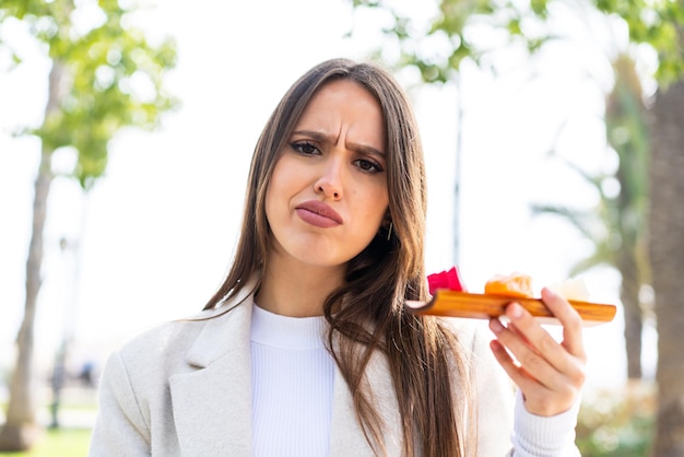 Mujer bonita joven sosteniendo sashimi al aire libre con expresión triste