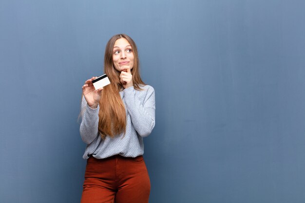 Mujer bonita joven con una tarjeta de crédito contra azul con un copyspace