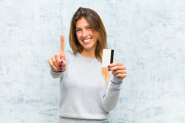 Mujer bonita joven con una tarjeta de crédito contra la pared del grunge