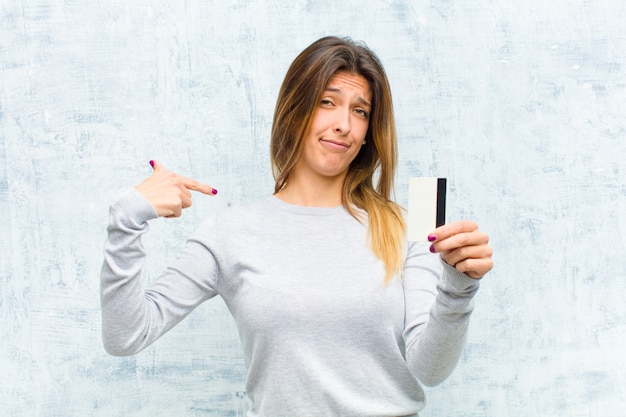 Mujer bonita joven con una tarjeta de crédito contra la pared del grunge