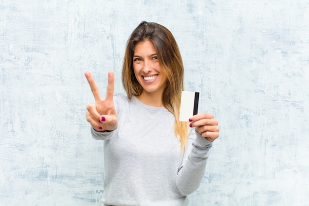 Mujer bonita joven con una tarjeta de crédito contra la pared del grunge