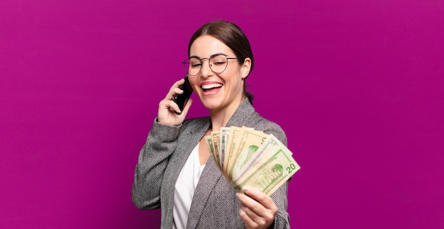 Mujer bonita joven con un teléfono y billetes de dólar.