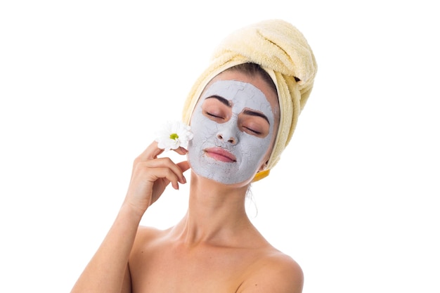 Foto mujer bonita joven con toalla amarilla en la cabeza y máscara cosmética en la cara con flor blanca