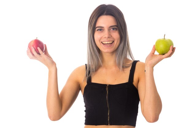 Mujer bonita joven en top negro sosteniendo dos manzanas sobre fondo blanco en estudio