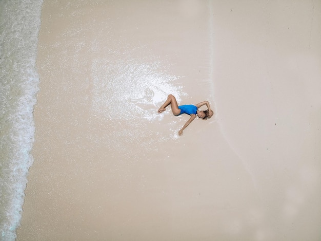 Mujer bonita joven en un traje de baño azul tumbado en una playa de arena durante la marea. Concepto de vacaciones de verano