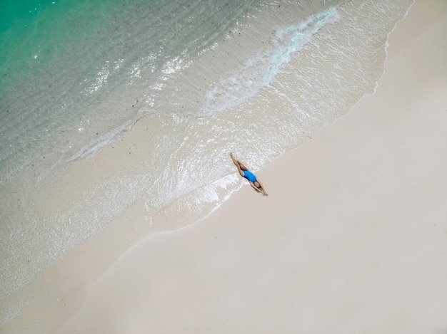 Mujer bonita joven en un traje de baño azul tumbado en una playa de arena durante la marea. concepto de vacaciones de verano