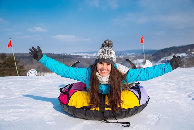 Mujer bonita joven en tubo de nieve levanta las manos hacia arriba deslizarse desde la colina de nieve