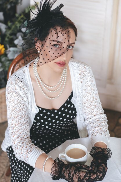 Mujer bonita joven vestida con estilo retro está sentada en el café de la calle con una taza de café