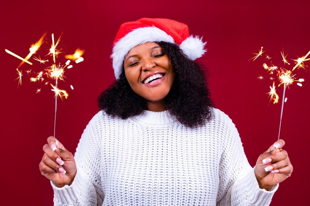 Mujer bonita latina alegre con máscara médica y sombrero rojo de santa claus riéndose aislada de fondo rojo, está feliz y emocionada llena de diversión